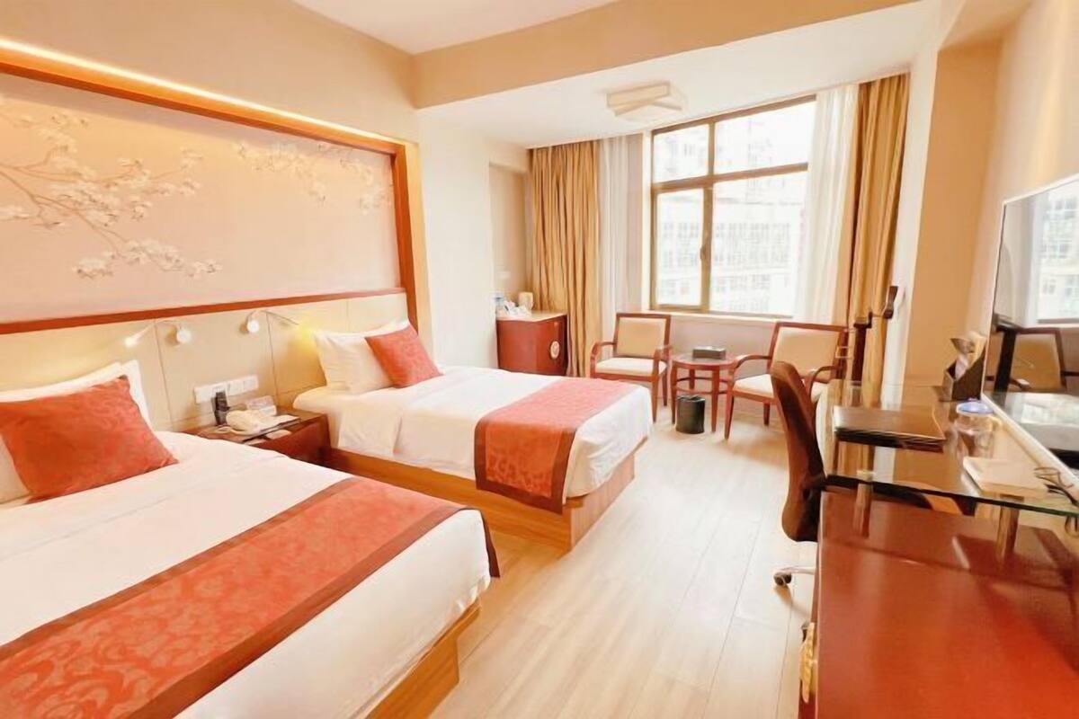 Habitación de hotel con dos camas, un escritorio, una silla, un televisor y una ventana con cortinas.