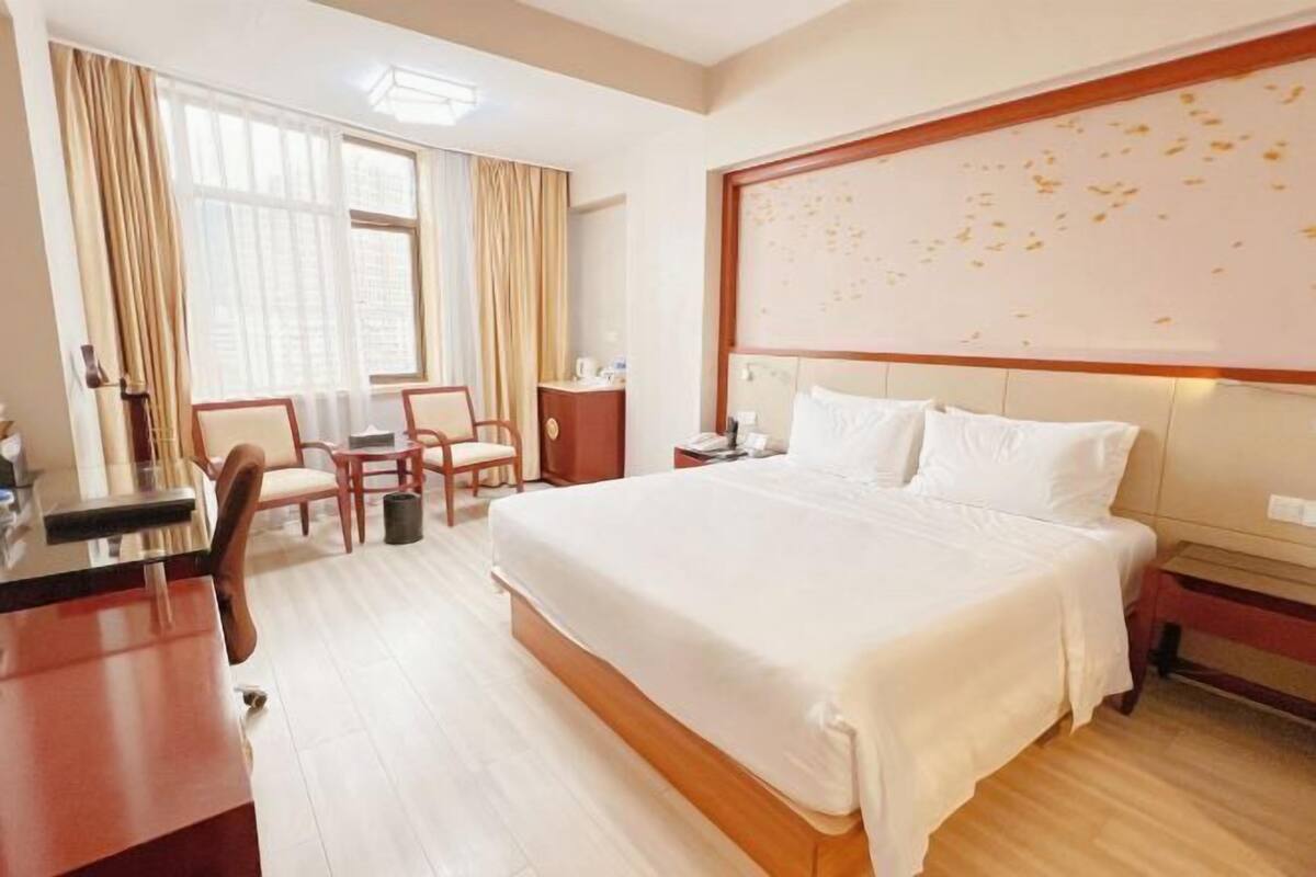 Una habitación de hotel con una cama grande, un escritorio, una silla y una ventana con cortinas.