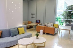 A modern hotel lobby with a grey sofa, orange armchairs, a white coffee table, and a large window offering a view of the city. - Jinhua Hotel (Huangshi)