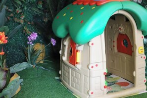 A small, enclosed playhouse with a green roof and a red door, surrounded by artificial plants. - Jinhua Hotel (Huangshi)