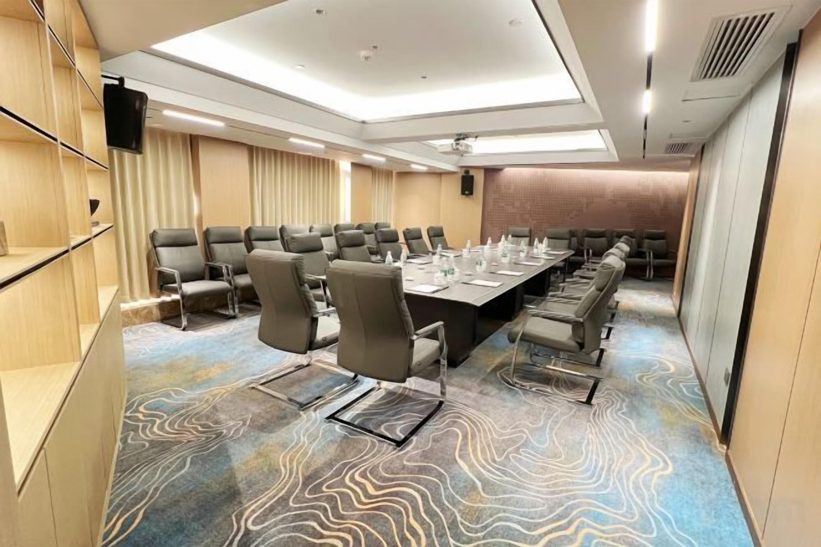 A conference room with a long table, multiple chairs, a flat-screen TV, and a patterned carpet.