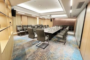 A conference room with a long table, multiple chairs, a flat-screen TV, and a patterned carpet.