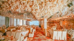 Un salón de banquetes con mesas redondas, decoración floral y una alfombra estampada.