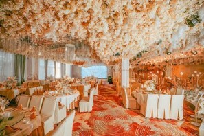 Un salón de banquetes con mesas redondas, decoración floral y una alfombra estampada.