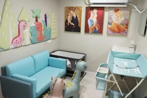 A pediatric room with a blue sofa, a play area with a toy dinosaur, and artwork on the walls. - Jinhua Hotel (Huangshi)