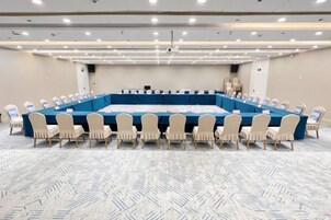 Un salón de conferencias con una gran mesa ovalada, sillas color beige y piso alfombrado.