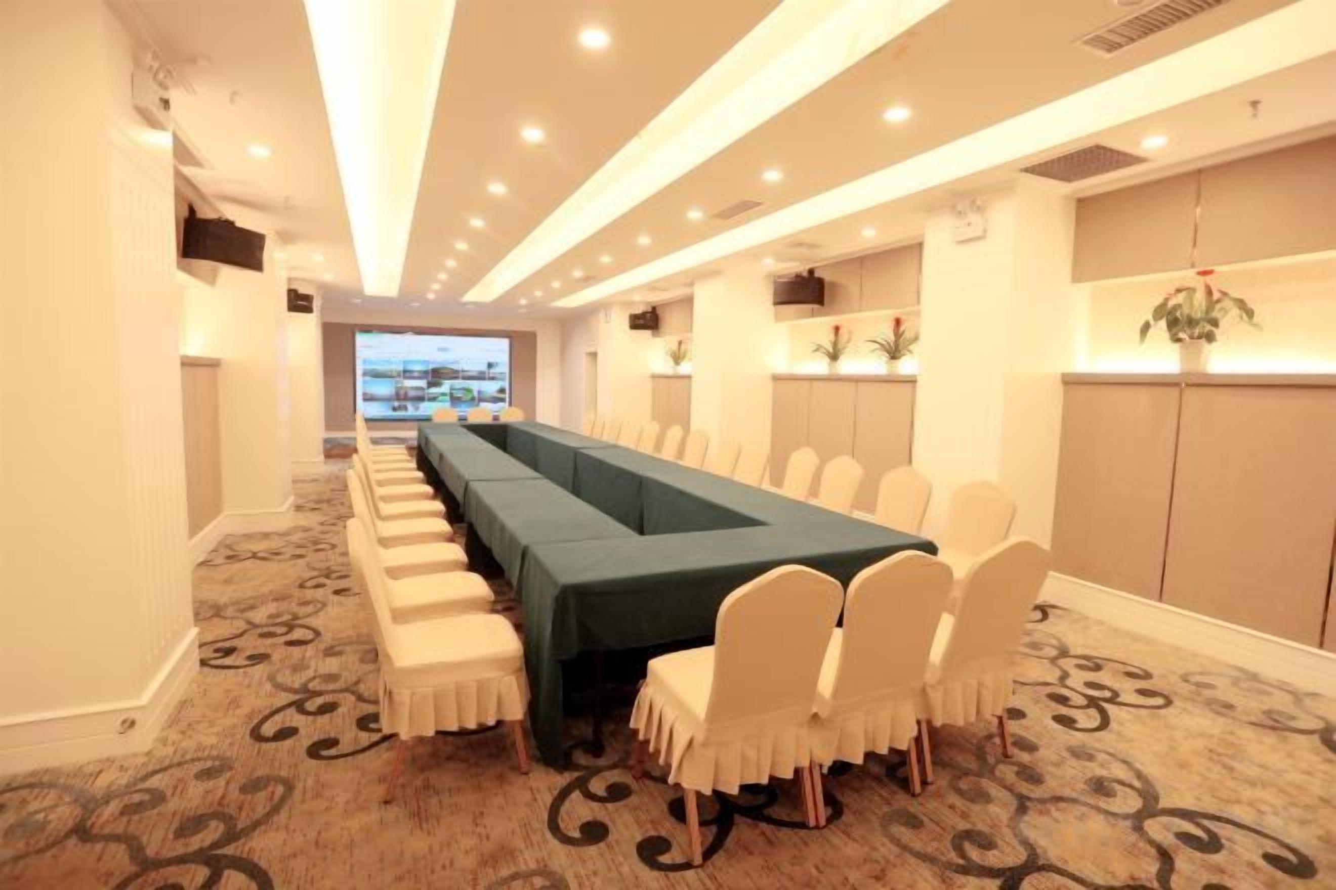 Un salón de conferencias con una larga mesa, sillas blancas y piso alfombrado.