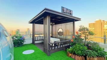 A rooftop garden with a wooden gazebo, green artificial grass, and a view of the city skyline.