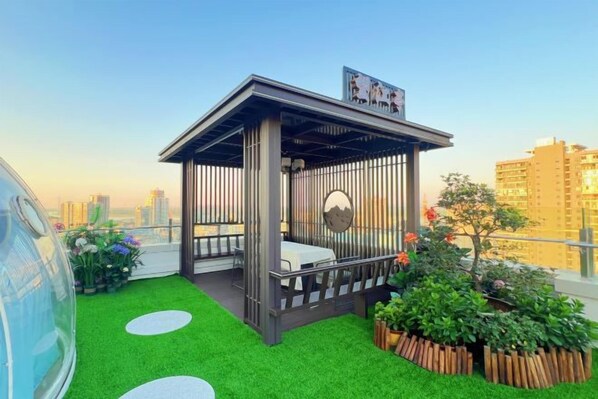 A rooftop garden with a wooden gazebo, green artificial grass, and a view of the city skyline. - Jinhua Hotel (Huangshi)