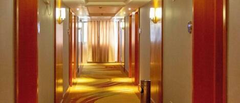 Un pasillo de hotel con suelo alfombrado, puertas a ambos lados e iluminación empotrada en las paredes.