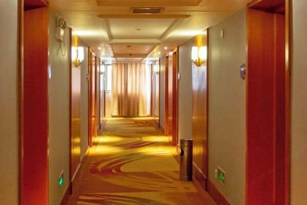 Un pasillo de hotel con suelo alfombrado, puertas a ambos lados e iluminación empotrada en las paredes.