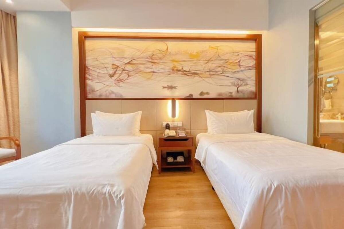 Habitación de hotel con dos camas individuales, una mesita de noche con lámpara y un cuadro abstracto grande en la pared.