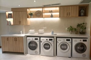 A laundry area with four washing machines, wooden cabinets, and a countertop with a sink and various items. - Jinhua Hotel (Huangshi)