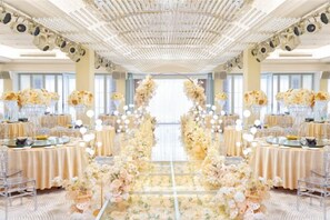 A banquet hall with a central aisle decorated with floral arrangements, tables set for a formal event, and a ceiling with a patterned design. - Jinhua Hotel (Huangshi)