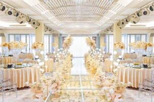 A banquet hall with a central aisle decorated with floral arrangements, tables set for a formal event, and a ceiling with a patterned design.