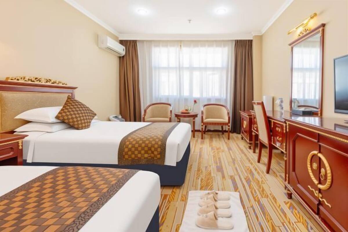 A hotel room with two beds, a desk, a chair, a TV, and a large mirror.