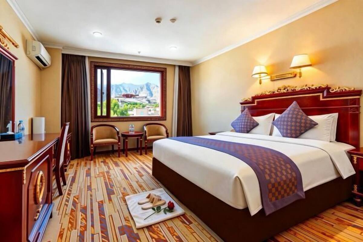 A hotel room with a large bed, a desk, a chair, a small table, and a window with a view.