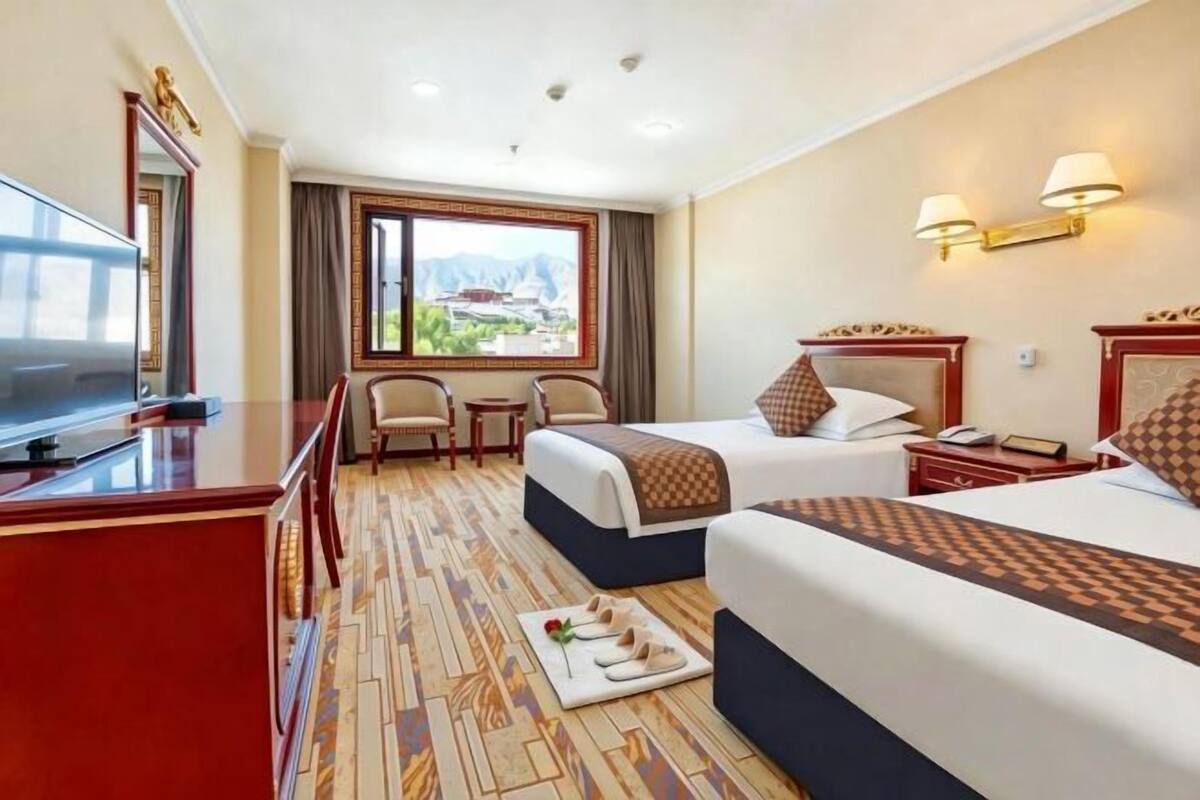 A hotel room with two beds, a TV, a desk, and a view of a mountainous landscape.