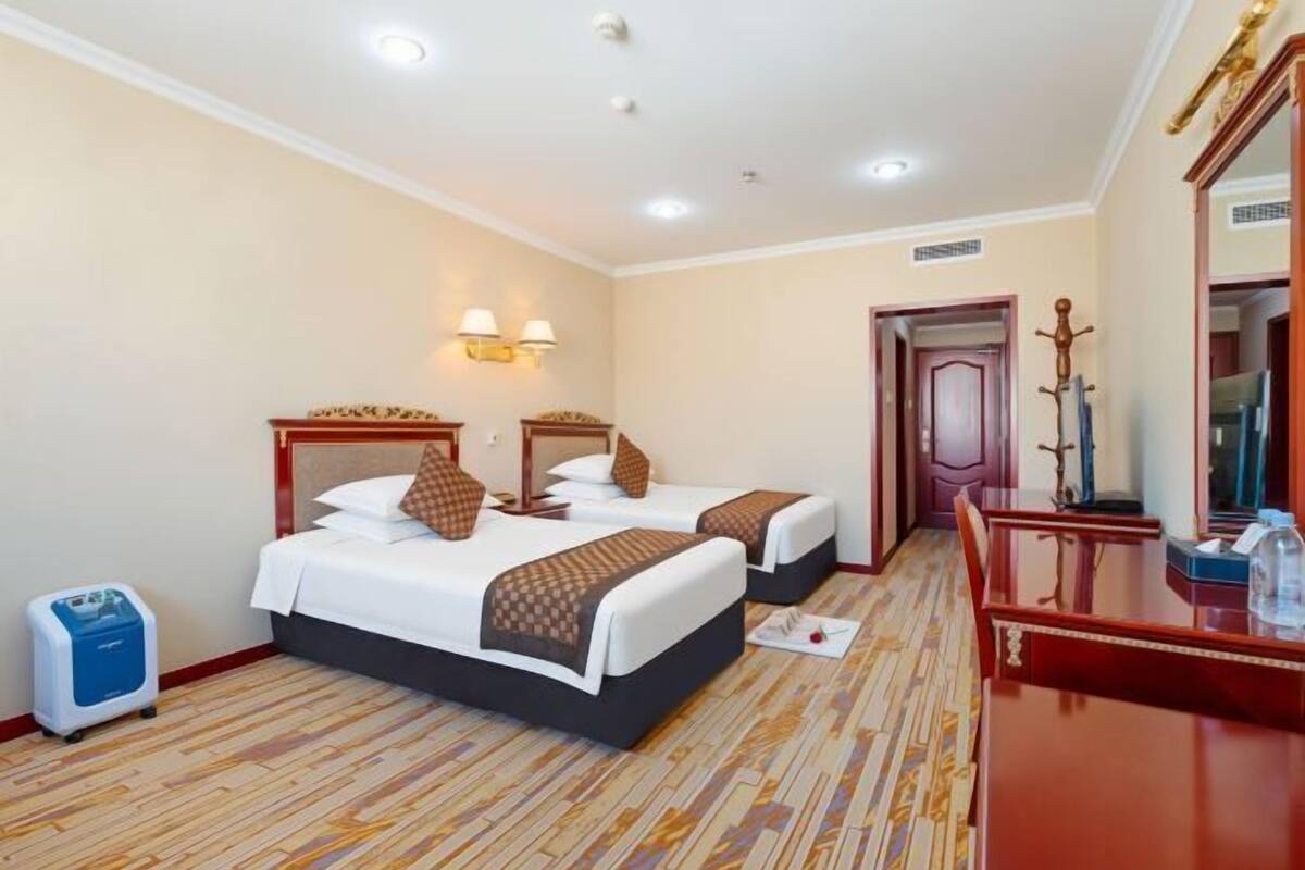 A hotel room with two beds, a wooden floor, a desk with a mirror, and a coat rack.