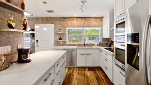 A modern kitchen with white cabinets, stainless steel appliances, and a wooden floor. - La Bougainvillea: 3BR, 2BA Home - Heated Pool (Fort Lauderdale)