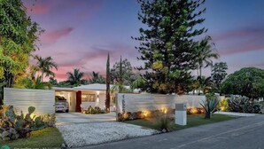 A modern house with a garage, surrounded by tropical vegetation and a large tree. - La Bougainvillea: 3BR, 2BA Home - Heated Pool (Fort Lauderdale)