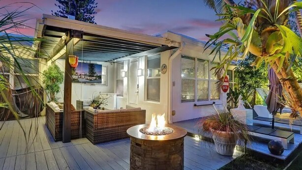 A modern outdoor living area with a fire pit, wooden deck, and potted plants. - La Bougainvillea: 3BR, 2BA Home - Heated Pool (Fort Lauderdale)