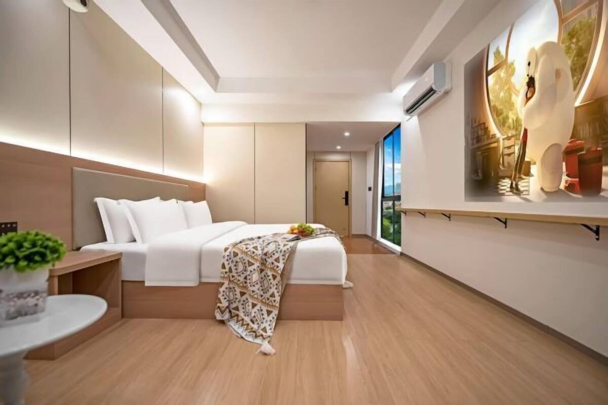 Habitación de hotel moderna con una cama grande, una mesita con una planta y un ventanal con vistas al exterior.