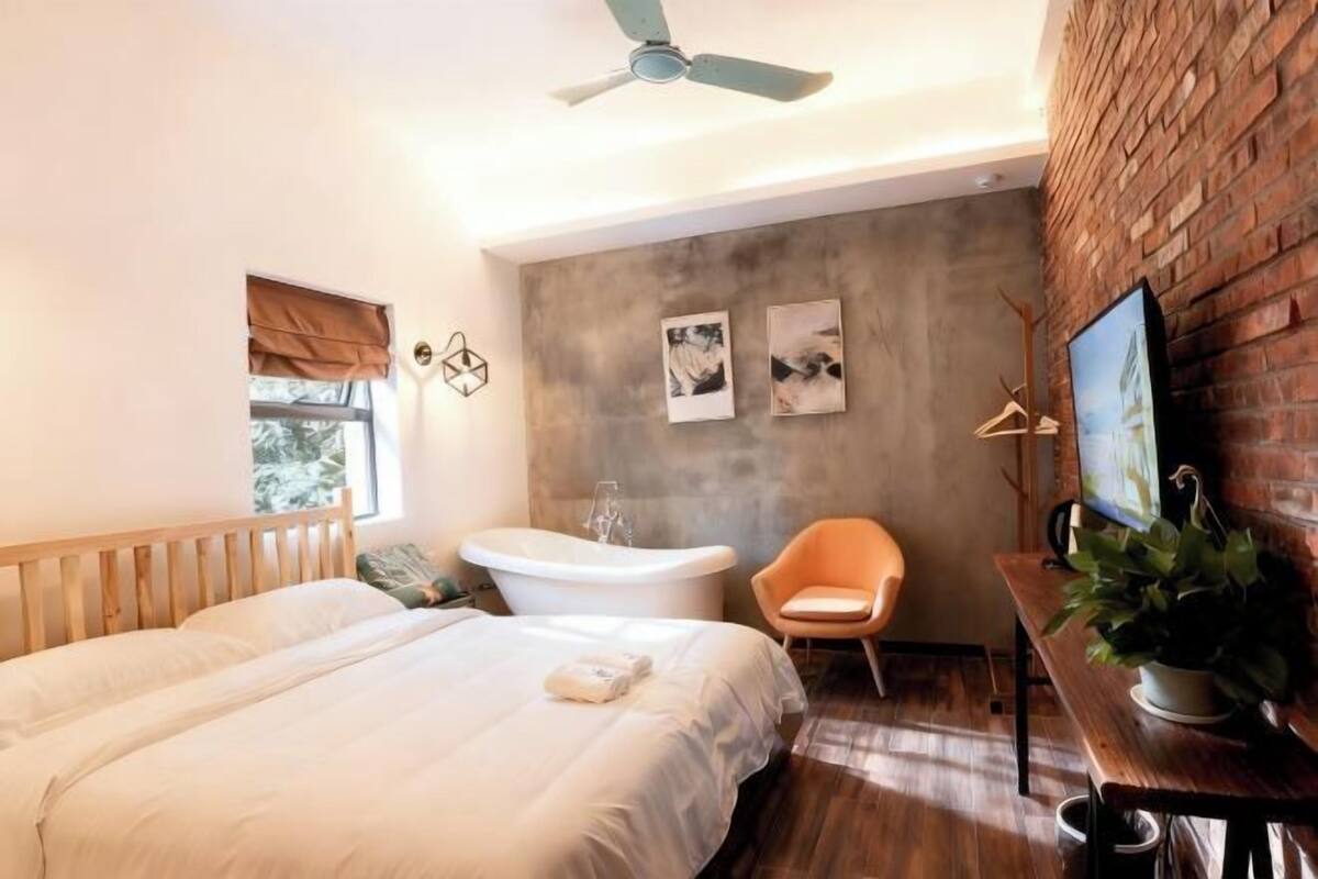 A modern bedroom with a large bed, a freestanding bathtub, a chair, and a TV on a wooden table.