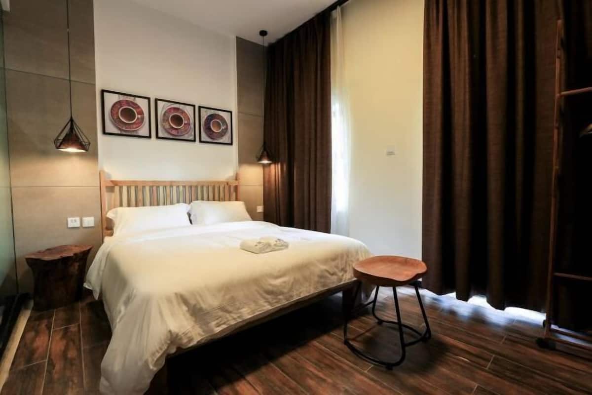 A modern hotel room with a large bed, a wooden nightstand, a round wooden stool, and two pendant lights.