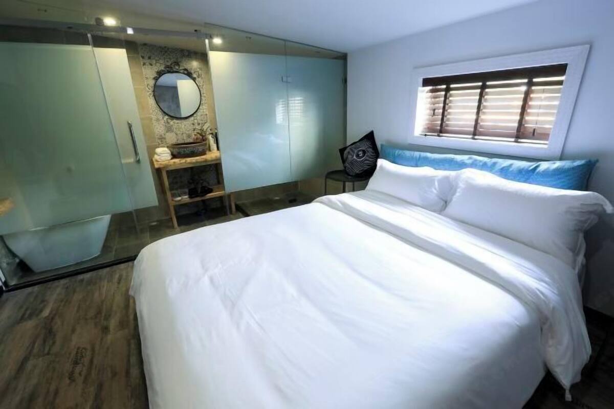 A bedroom with a large bed, a wardrobe, a mirror, and a window with blinds.