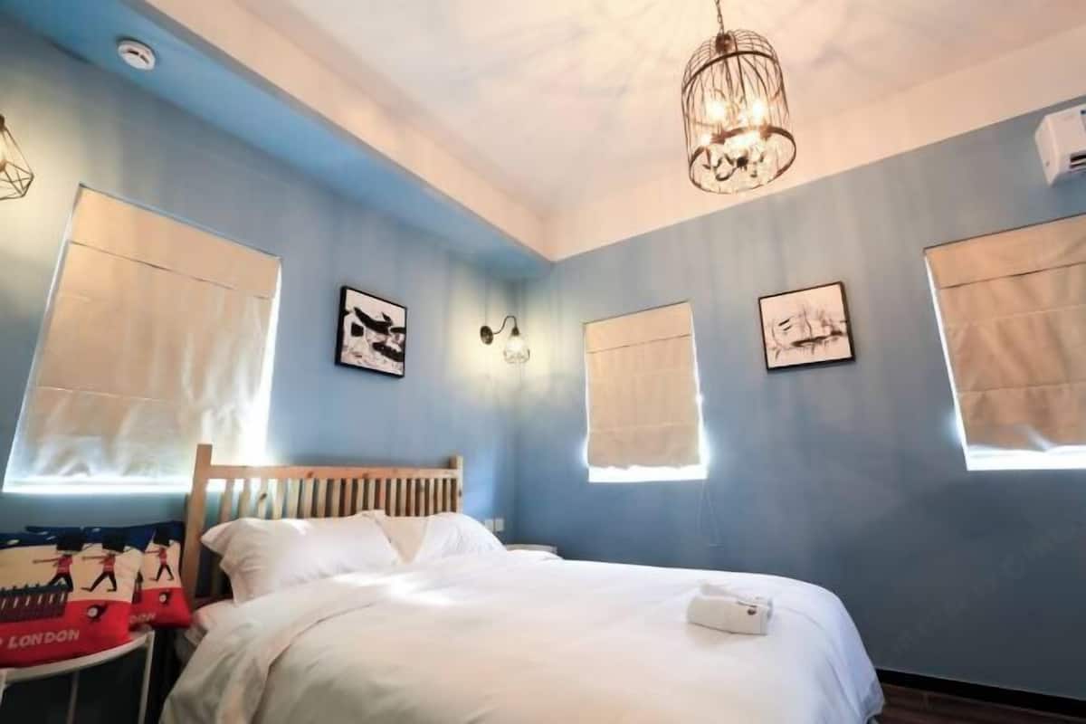 A bedroom with a bed, a wooden headboard, a hanging light fixture, and artwork on the walls.
