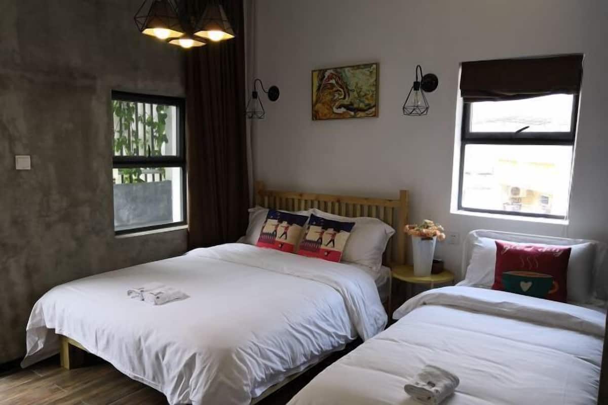 A room with two beds, a wooden headboard, a small table with a vase of flowers, and a painting on the wall.
