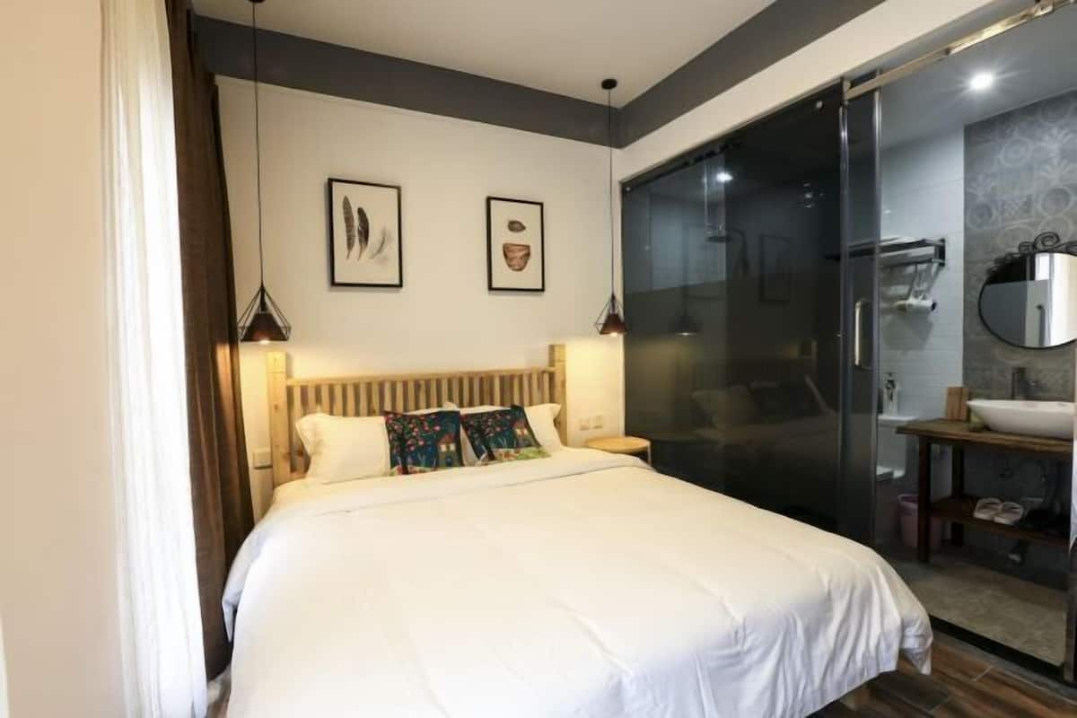 A modern hotel room with a large bed, a glass shower enclosure, and a bathroom with a sink and mirror.