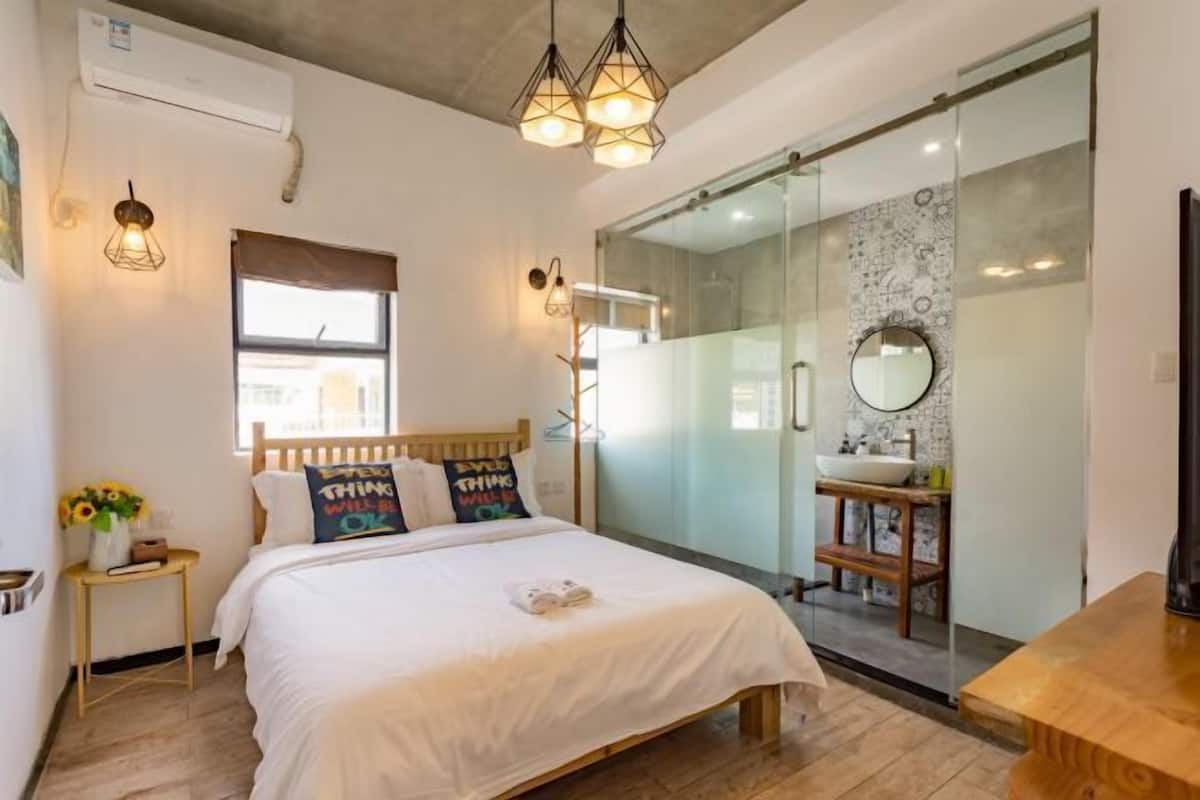 A bedroom with a wooden bed, a bedside table with a vase of flowers, and a window with a view.