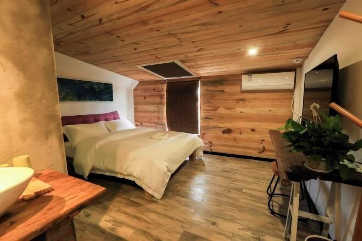 A wooden-paneled room with a bed, a small table with a bowl, and a potted plant.