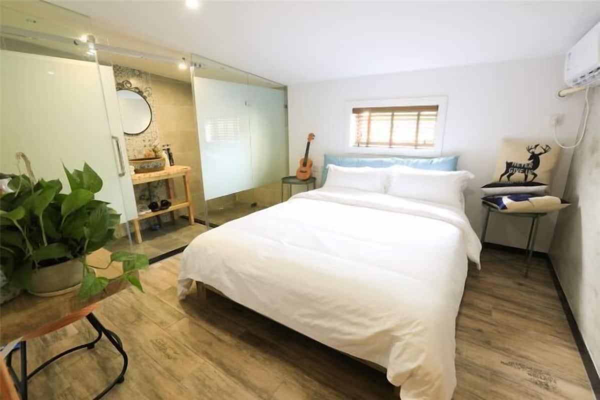 A bedroom with a large bed, a guitar, a mirror, and a window with blinds.