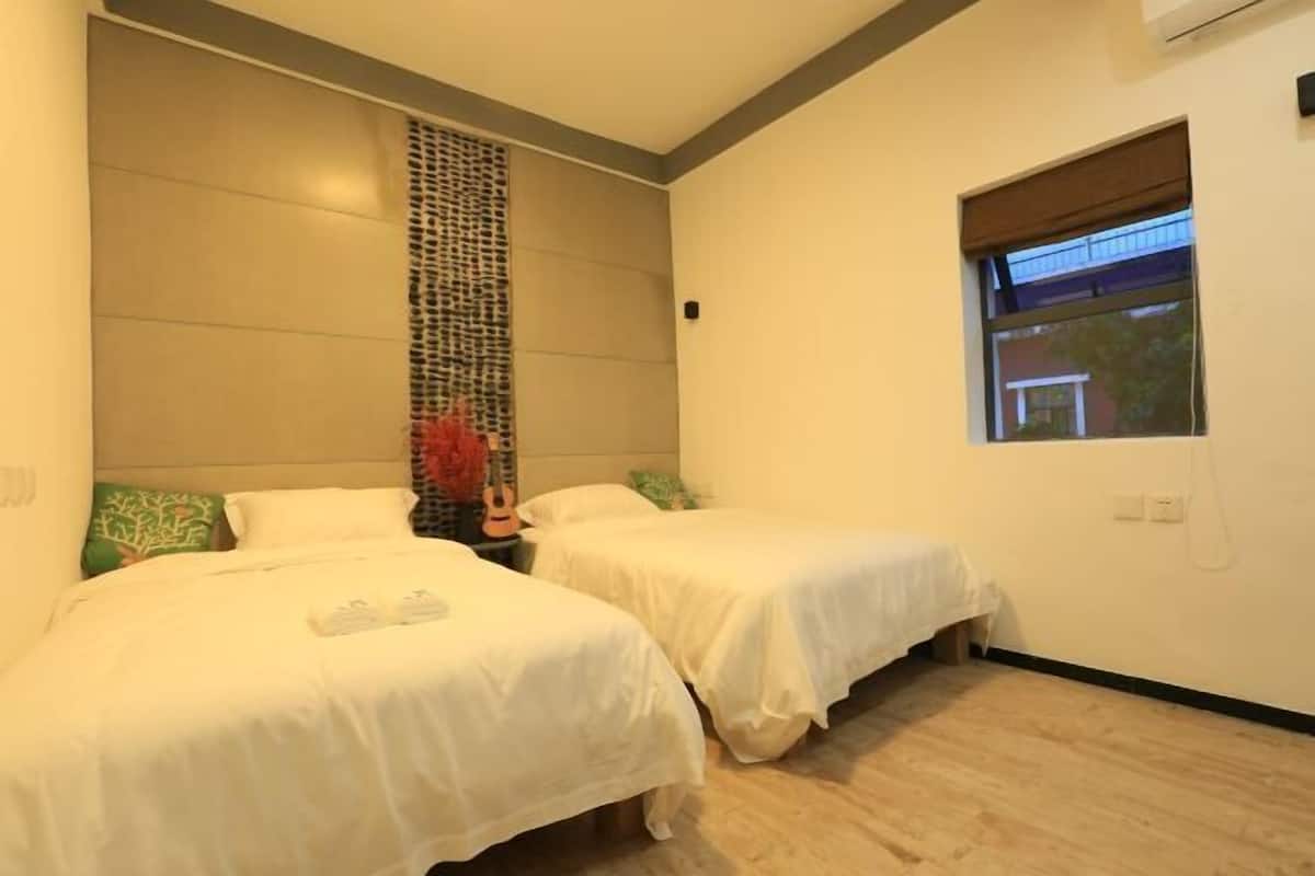 A bedroom with two beds, a window, and a wall-mounted air conditioner.