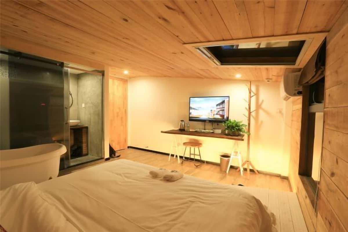 A cozy bedroom with a bed, a television, a small kitchen area, and a wooden ceiling.