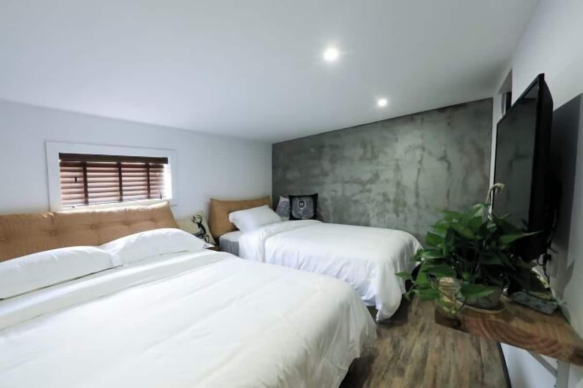 A bedroom with two beds, a large wall-mounted TV, and a window with blinds.