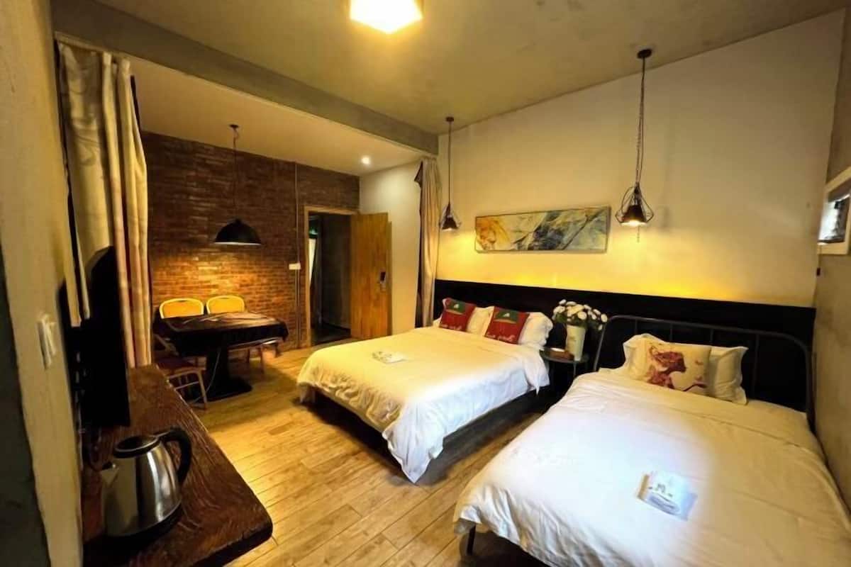 A hotel room with two beds, a wooden floor, a brick wall, a painting, and a table with chairs.