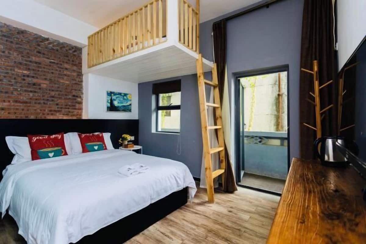A bedroom with a loft bed, a wooden ladder, a desk, and a view of the outdoors.