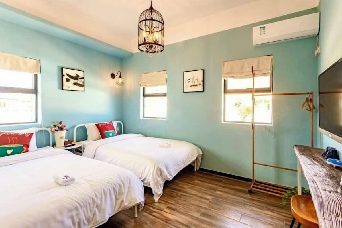 A room with two beds, a wooden floor, a hanging light fixture, and a television on a wooden table.