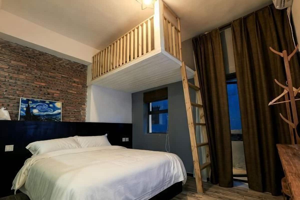 A bedroom with a bunk bed, a brick wall, a painting, a window with curtains, and a wooden ladder.