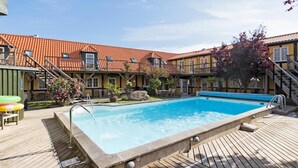 En swimmingpool med en træterrasse, omgivet af en bygning med et flis tag og flere balkoner.