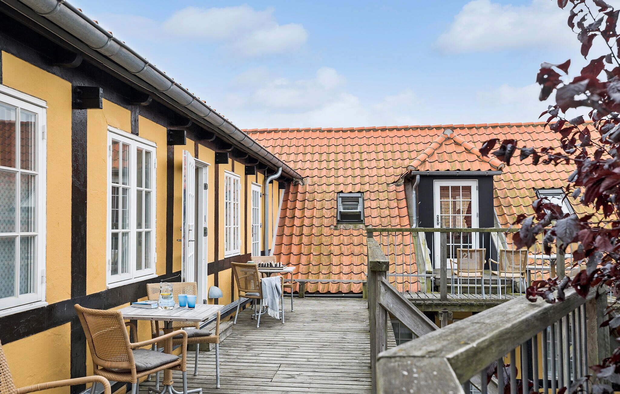 Een binnenplaats met buiten zitplaatsen, een houten terras en een gebouw met oranje pannendaken.