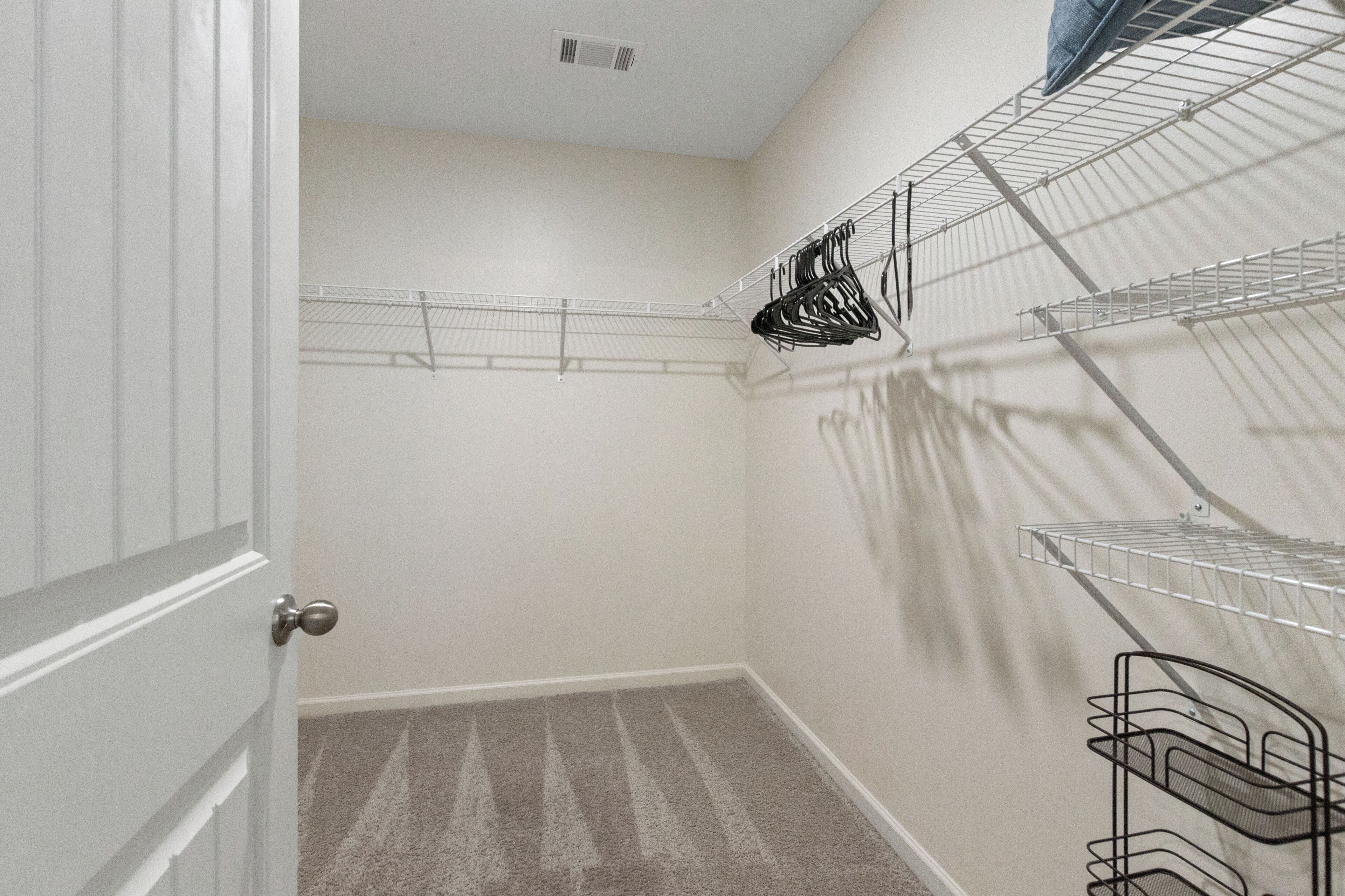 A corner of a room with a white door, a beige carpet, and metal wire shelves against the wall.