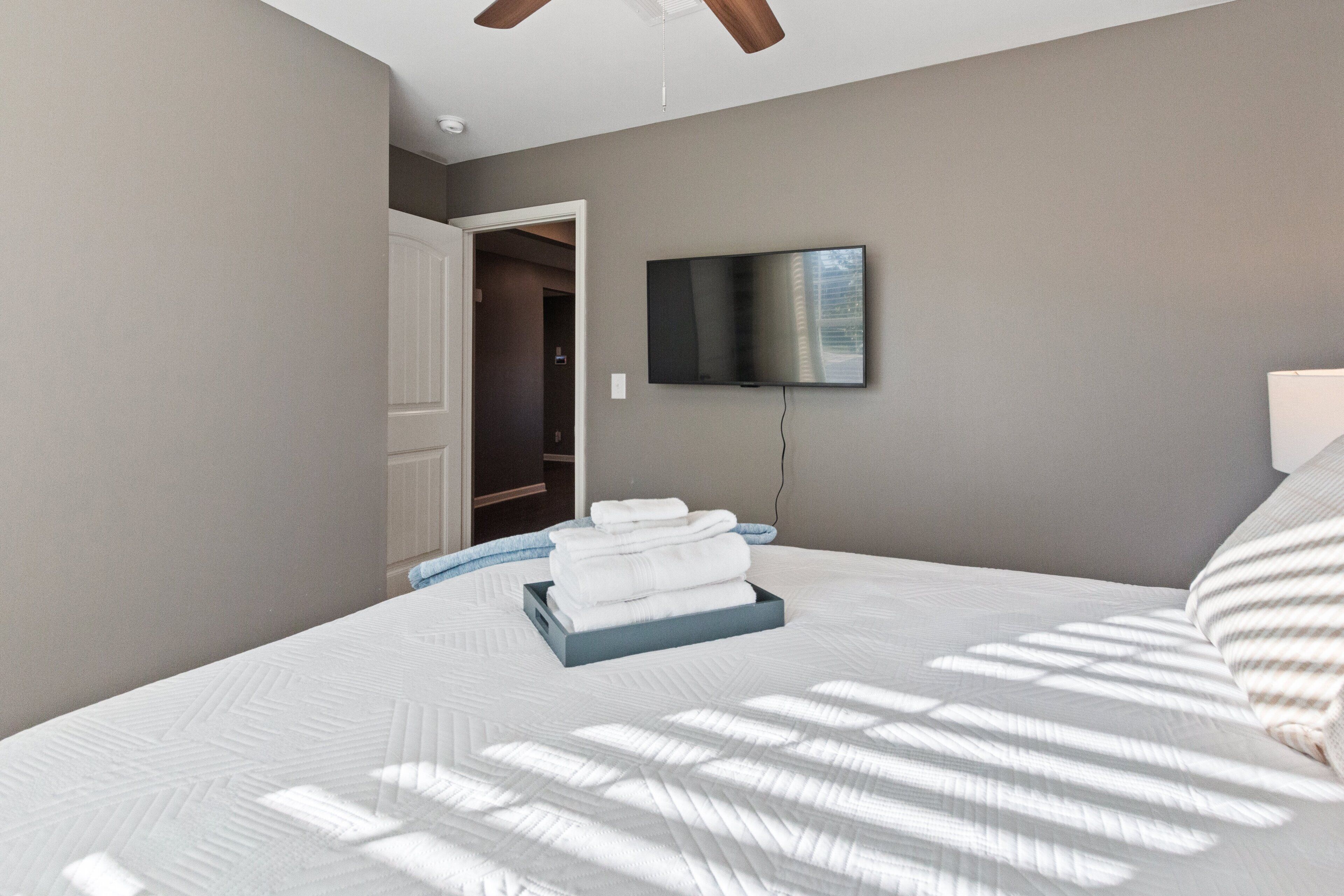 Un dormitorio con una cama, un televisor instalado en la pared y una puerta que da a un armario.