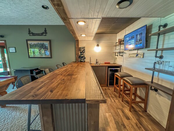 A wooden bar area with stools, a refrigerator, and a TV mounted on the wall.