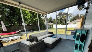 A covered patio with wicker furniture, a red hammock, and a view of the backyard. - It's beach time! Enjoy the sunshine! (Ormond Beach)