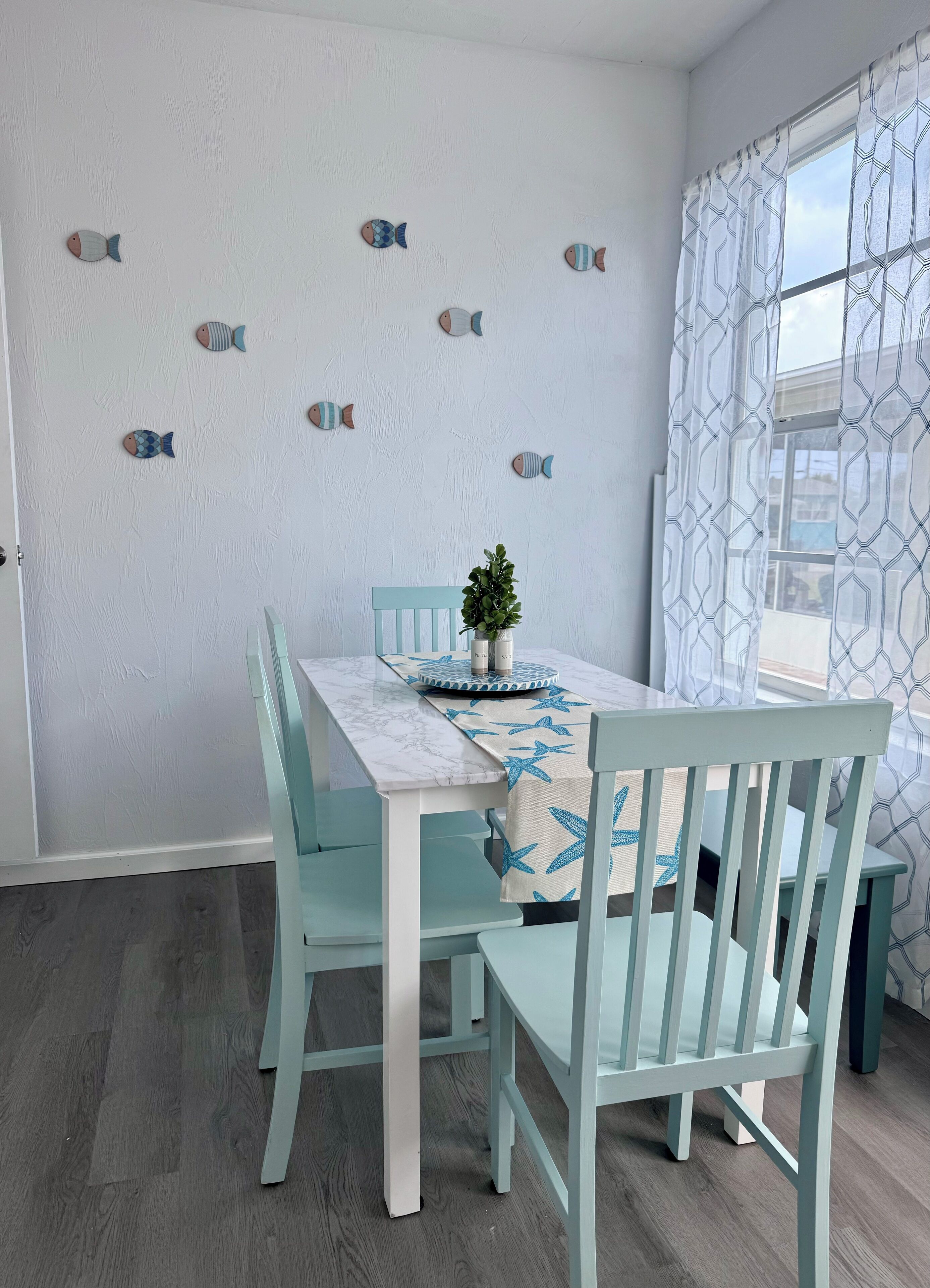A dining area with a white table, teal chairs, and a wall decorated with fish decals.